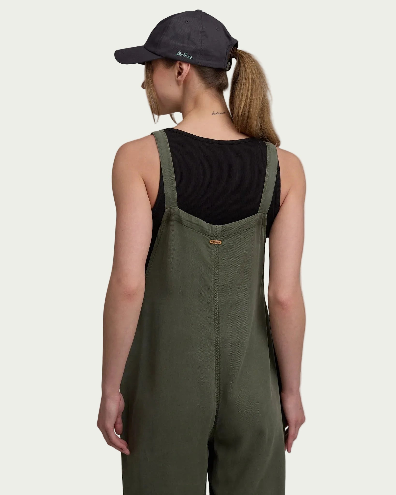 Olive green jumpsuit with adjustable straps shown from back, worn with black tank top