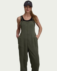 Olive green jumpsuit with adjustable straps and front pockets worn by woman with baseball cap