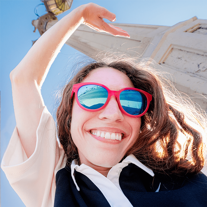 Woman wearing oversized round sunglasses with red frames and blue mirrored lenses, smiling outdoors