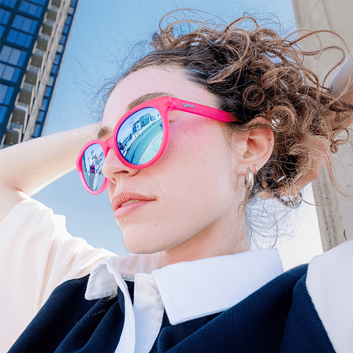 Model wearing oversized round sunglasses with bright pink frames and blue mirrored lenses outdoors