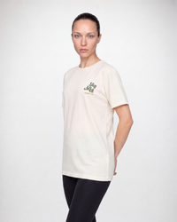 Cream unisex crew neck t-shirt with small chest logo, worn by female model, three-quarter view
