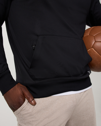 Close-up detail of black pullover hoodie kangaroo pocket with zipper, model holding football