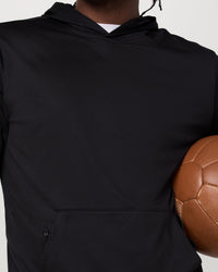 Black pullover hoodie detail shot, model holding a brown soccer ball, front pocket visible