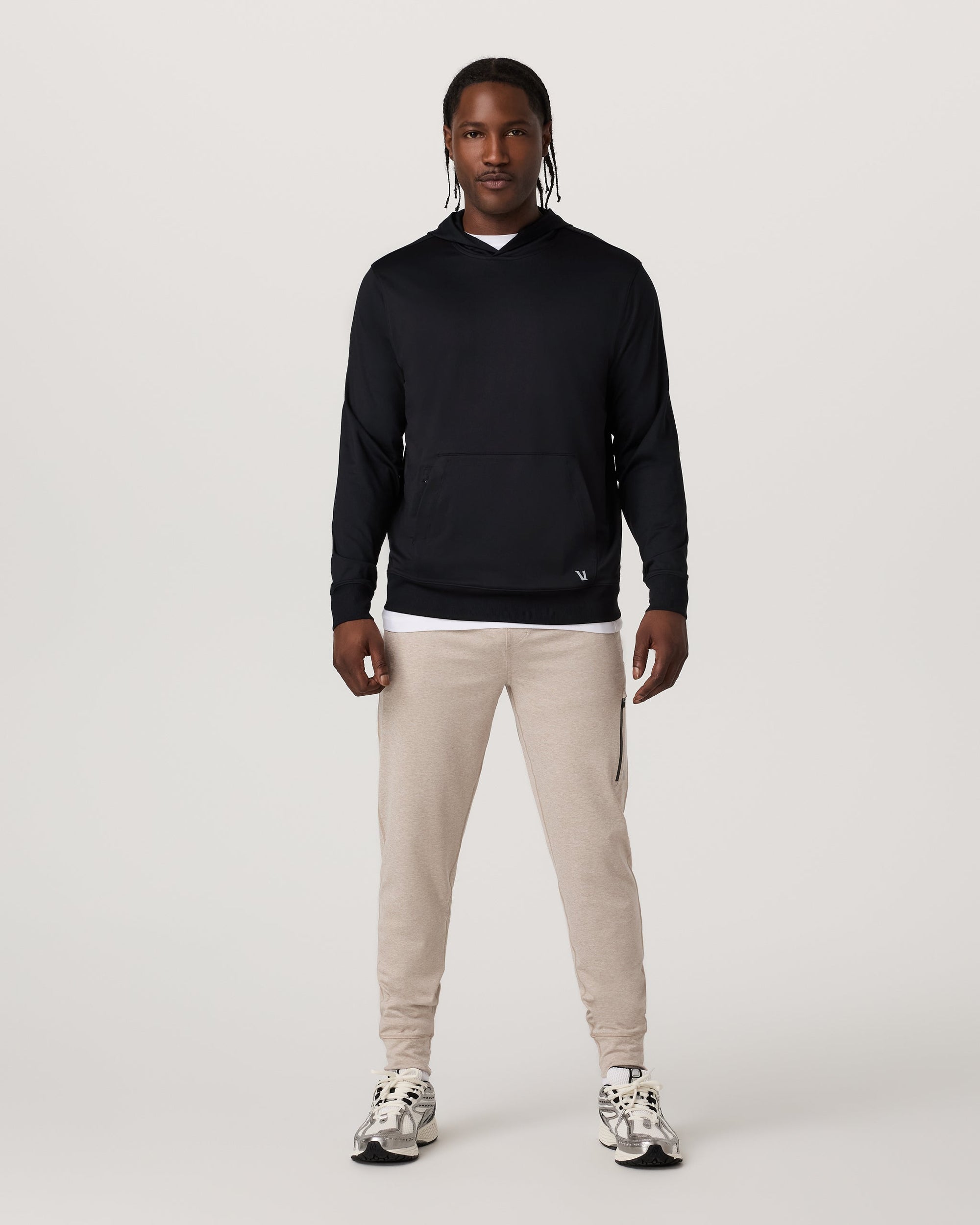Men's black pullover hoodie with kangaroo pocket, worn with beige joggers, front view