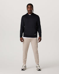 Men's black pullover hoodie with kangaroo pocket, worn with beige joggers, front view
