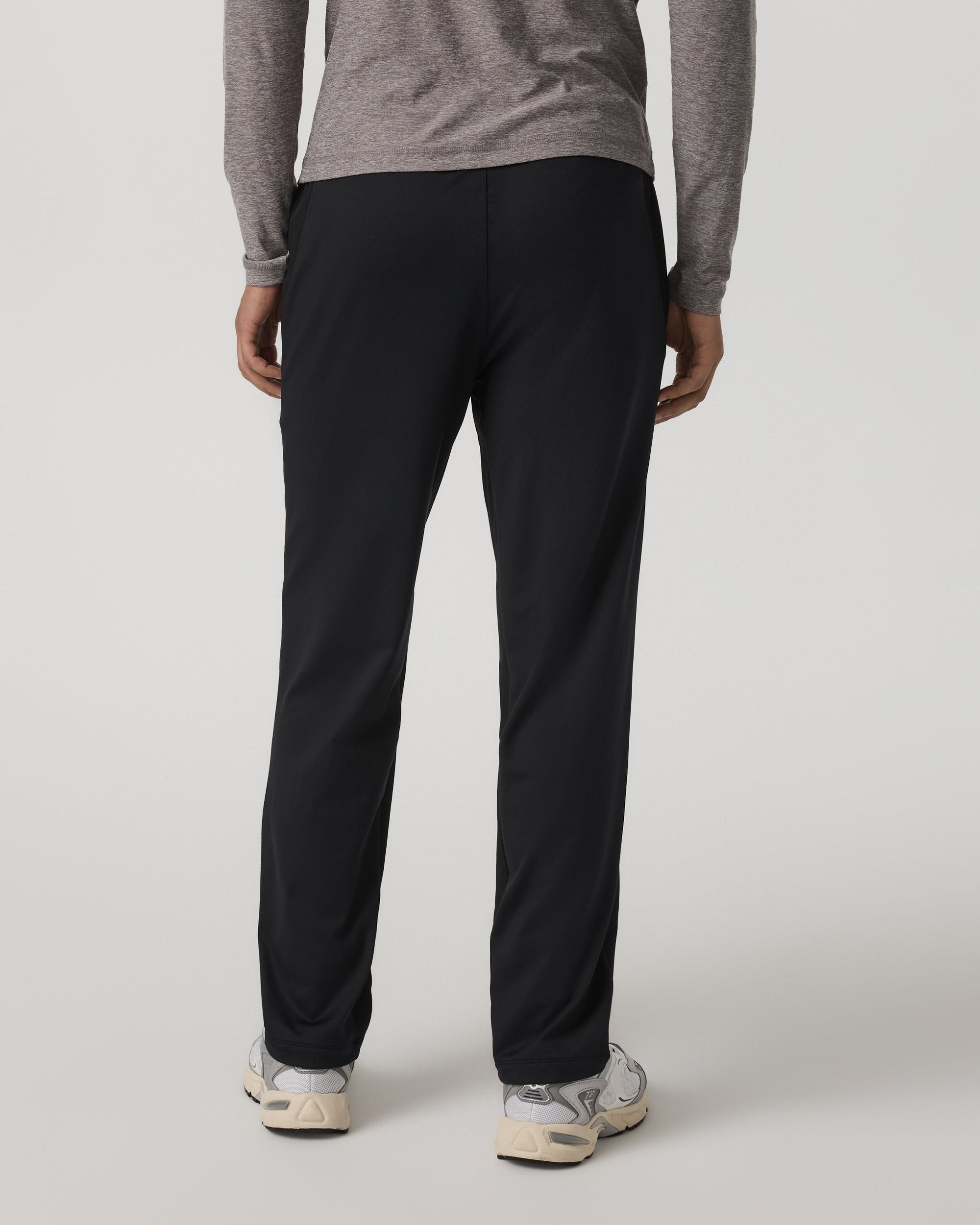 Men's black track pants back view, slim fit with clean seams, worn with white sneakers
