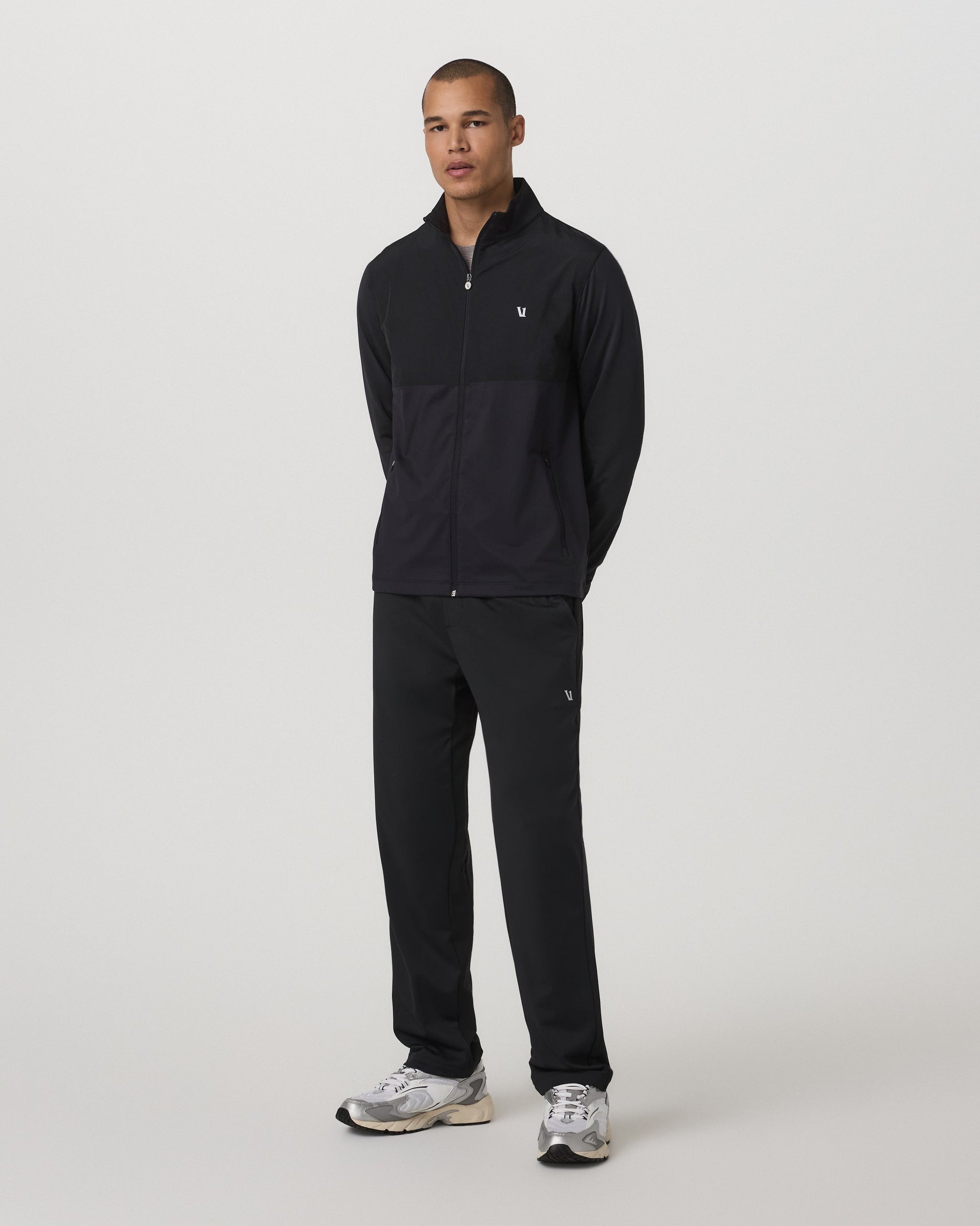 Black straight-leg track pants with small logo detail, worn with matching zip jacket, front view
