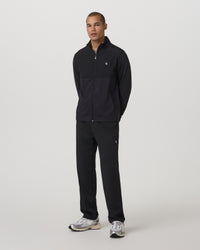 Black straight-leg track pants with small logo detail, worn with matching zip jacket, front view