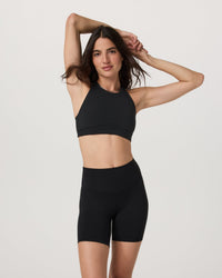 High neck sports bra in black, front view on model, paired with matching bike shorts