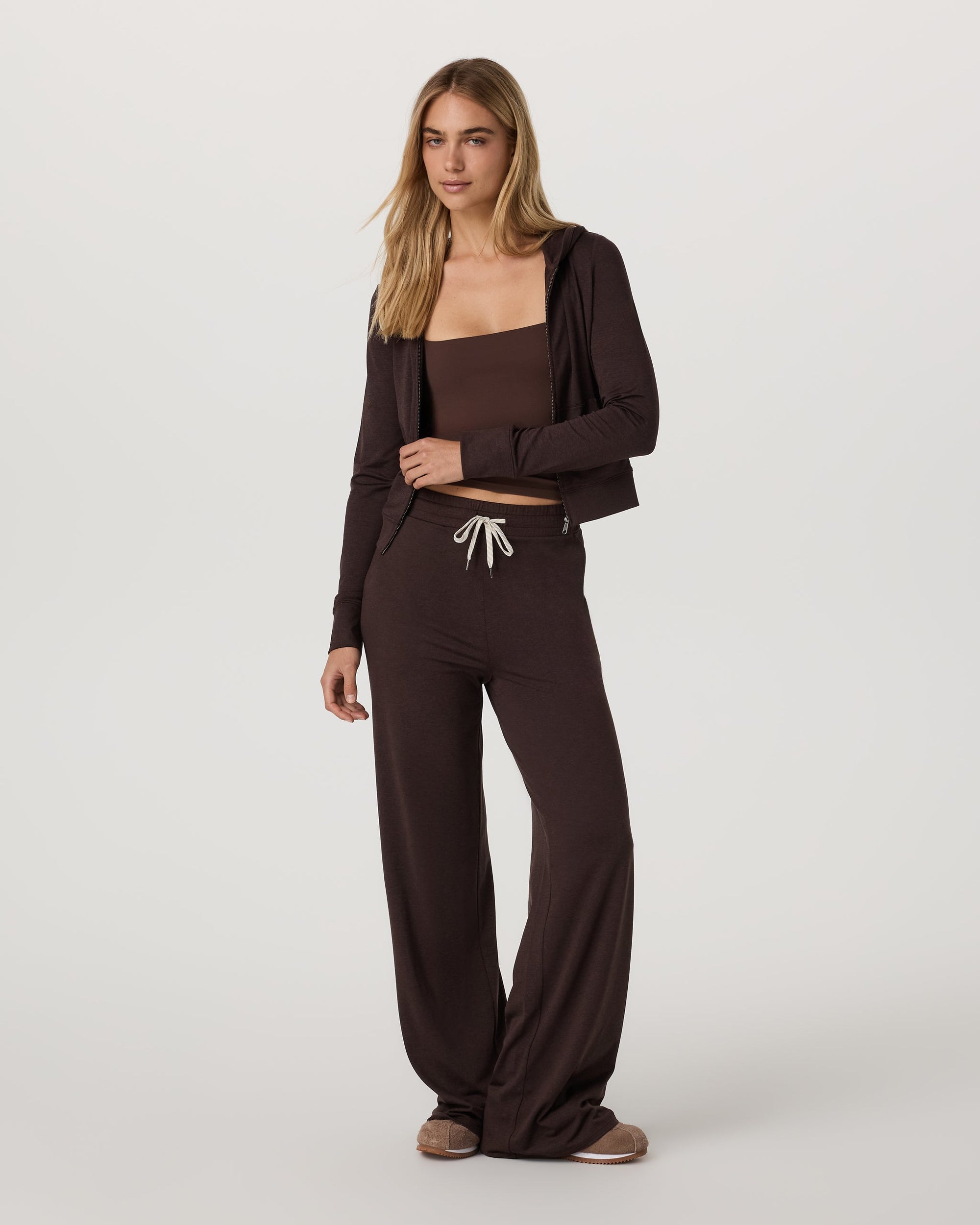 Women's cropped full-zip hoodie in dark brown, worn open over matching tube top and wide-leg pants