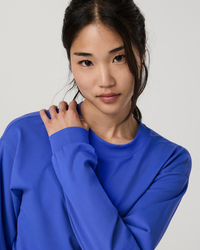 Woman wearing a bright blue crewneck sweatshirt, close-up detail shot showing neckline and cuffs