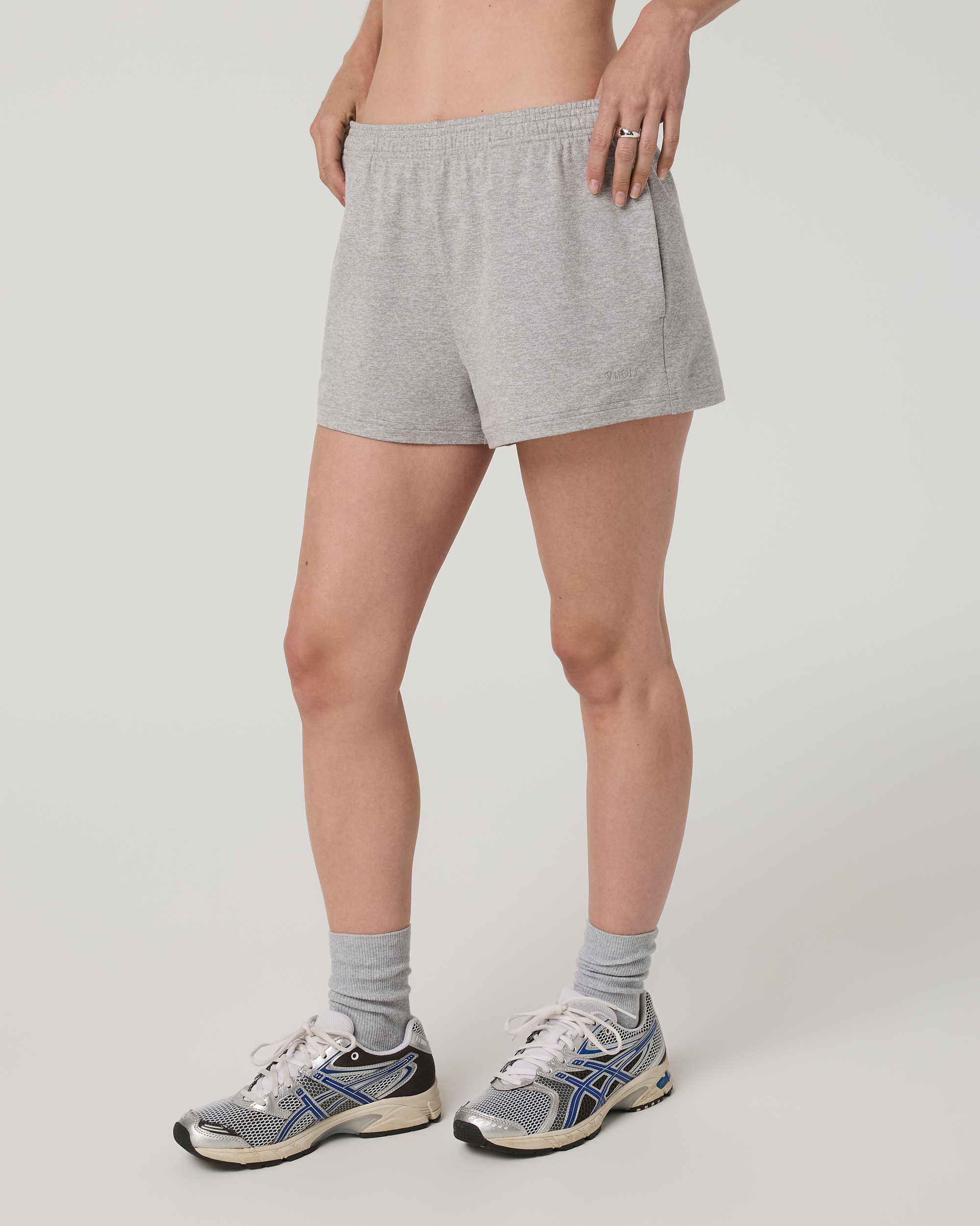 Women's grey heather athletic shorts with elastic waistband, side view on model with sneakers