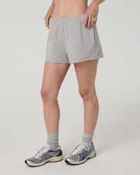 Women's grey heather athletic shorts with elastic waistband, side view on model with sneakers