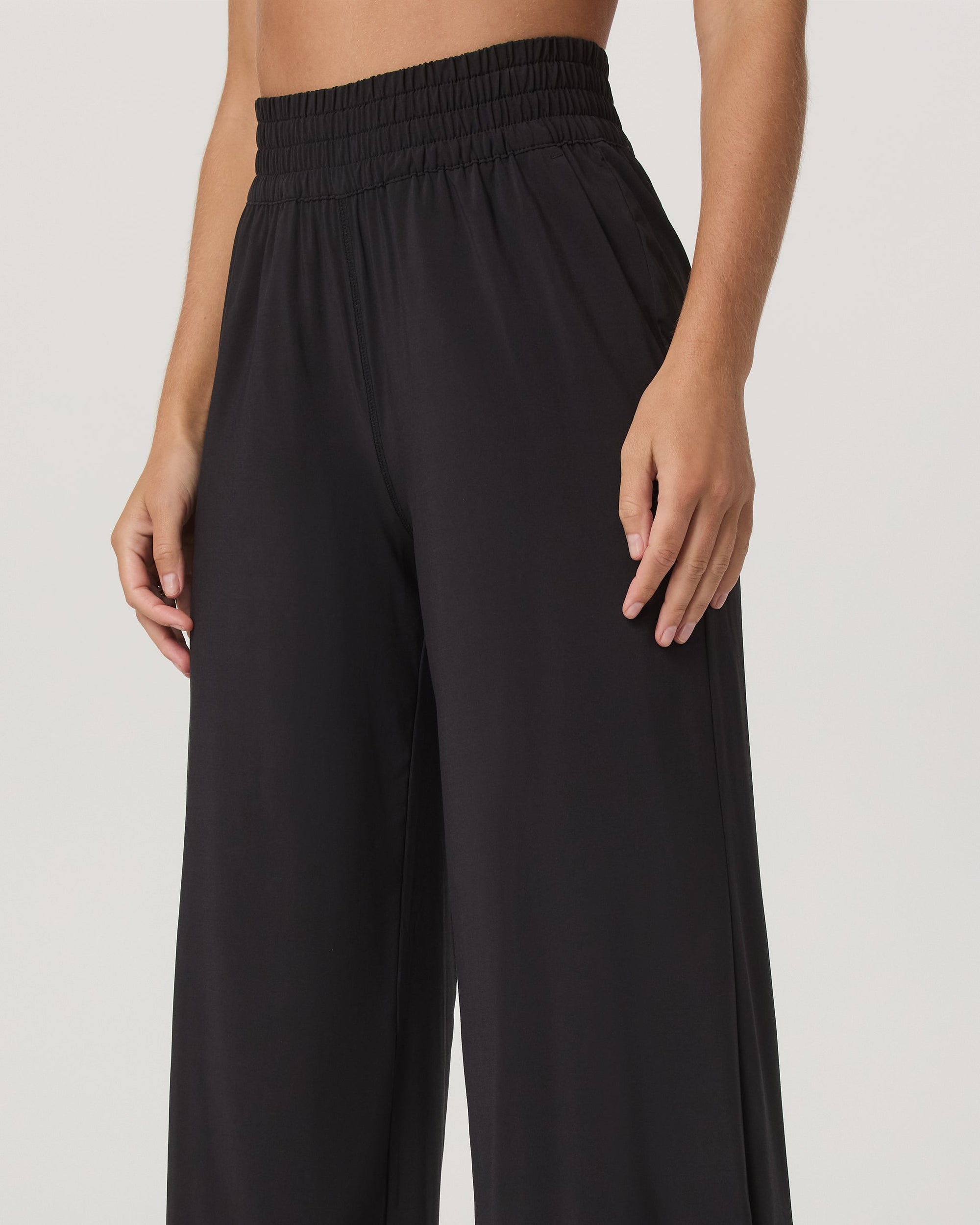 Close-up detail of wide-leg black pants with smocked elastic high waistband, on model