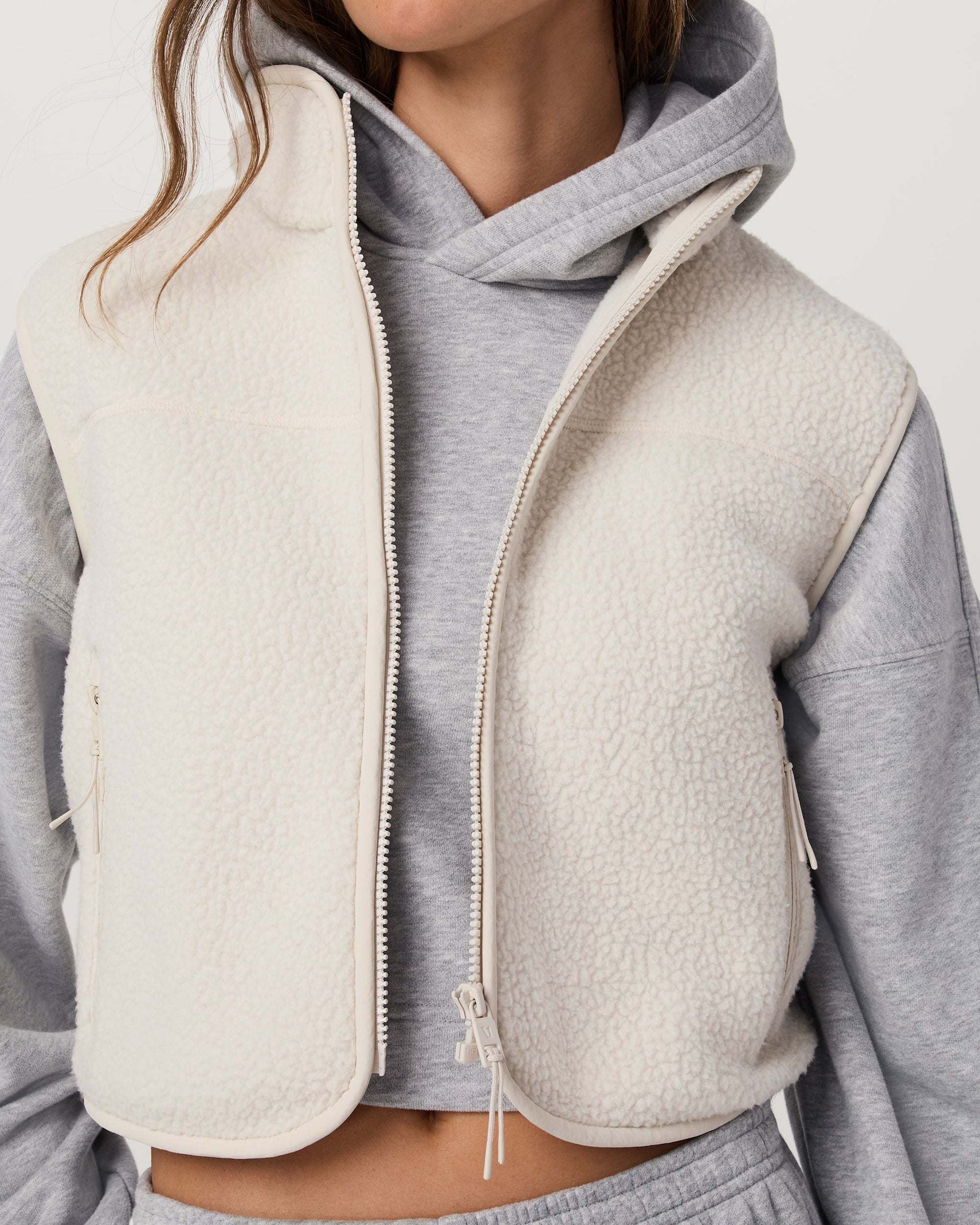 Cropped sherpa fleece vest with full zip, worn over gray hoodie, detail view