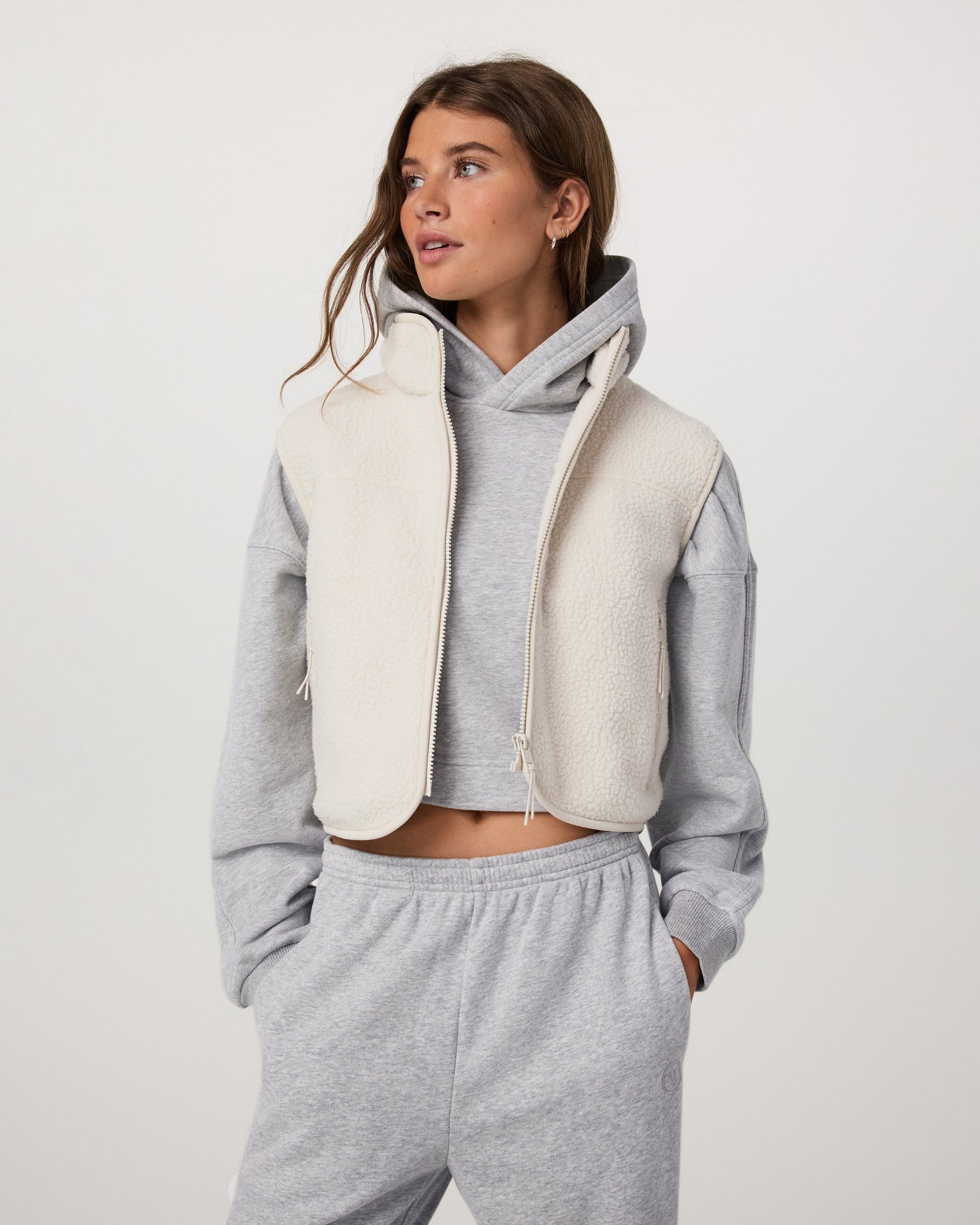 Women's cropped sherpa fleece vest with full zip, worn over gray hoodie, front view