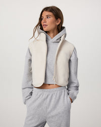 Women's cropped sherpa fleece vest with full zip, worn over gray hoodie, front view
