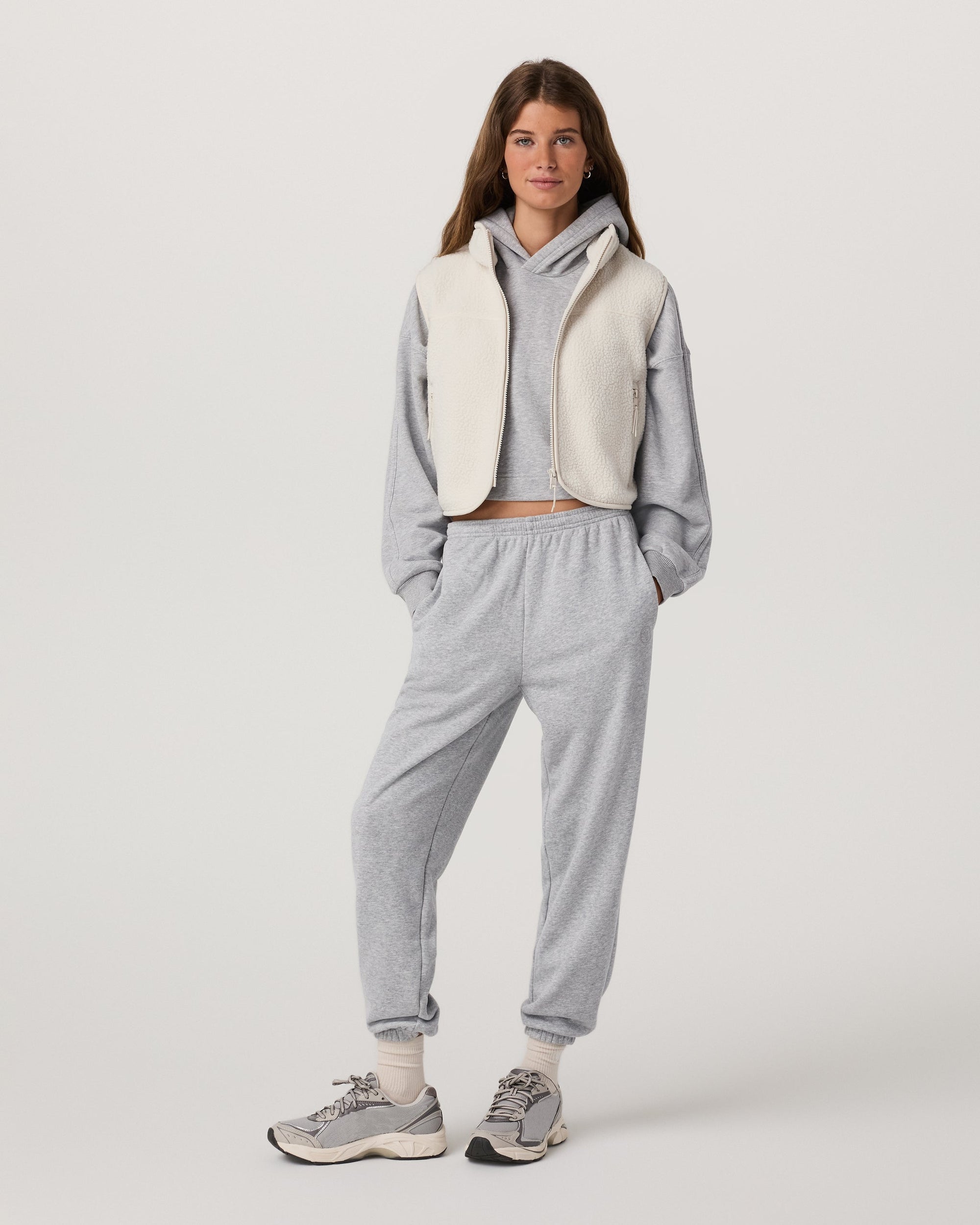 Women's cropped sherpa fleece vest with zip front, worn over gray hoodie, full front view