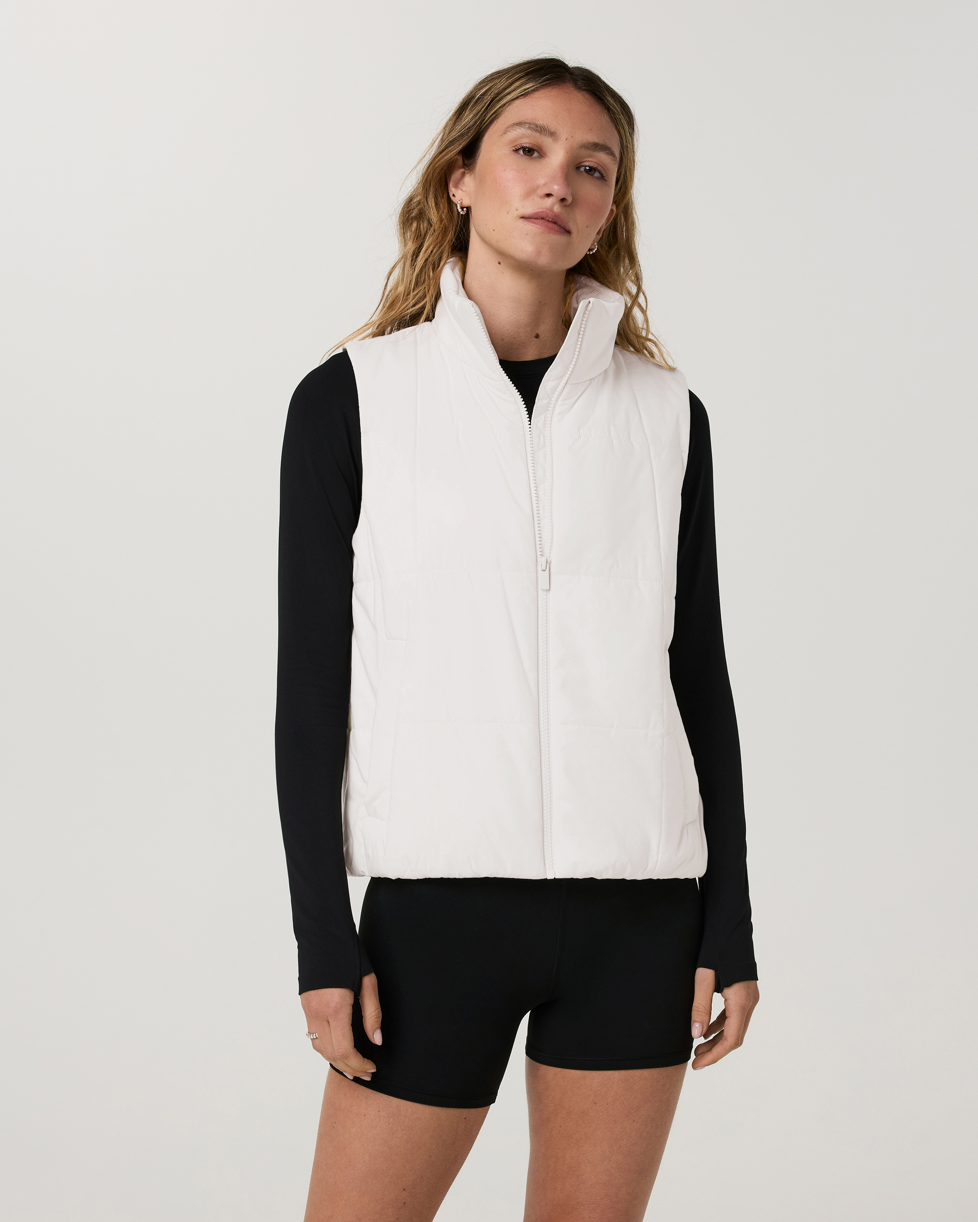 Women's white puffer vest with stand collar and zip front, layered over black long sleeve, front view