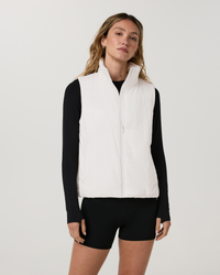 Women's white puffer vest with stand collar and zip front, layered over black long sleeve, front view
