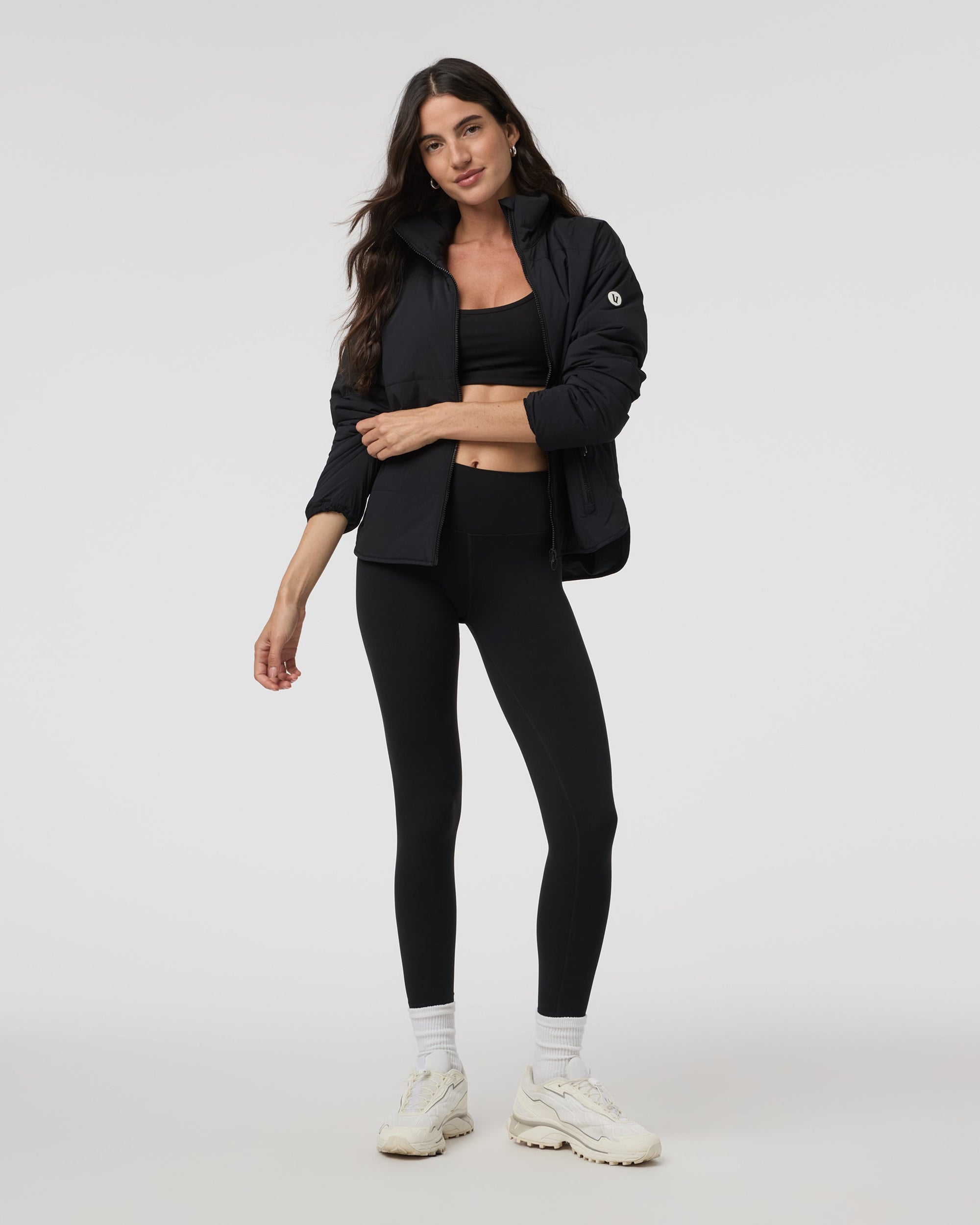 Black insulated puffer jacket with stand collar, worn open over matching sports bra and leggings
