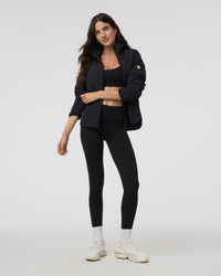 Black insulated puffer jacket with stand collar, worn open over matching sports bra and leggings