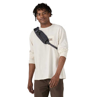 Man wearing a small dark navy crossbody sling bag over a cream long-sleeve shirt