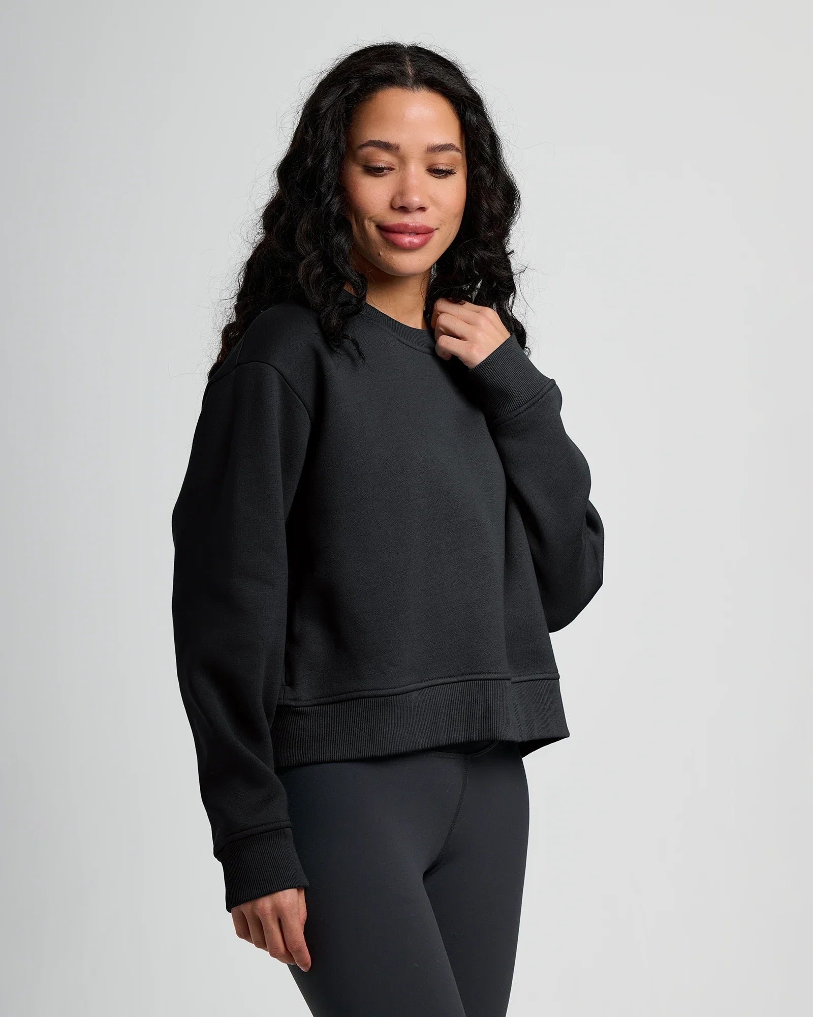 Woman wearing dark fleece crew sweatshirt with ribbed cuffs and hem, three-quarter view