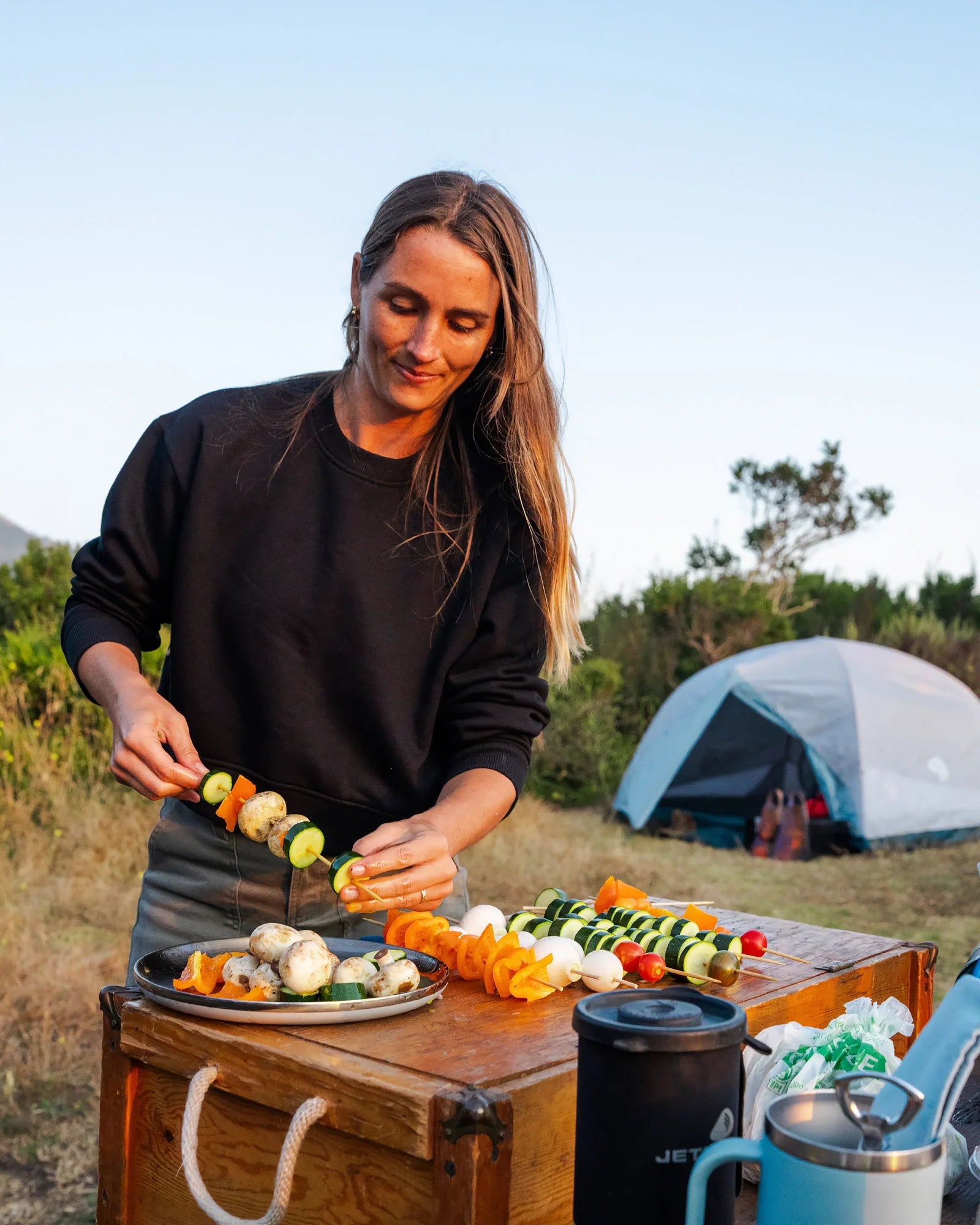 Woman wearing black fleece crew sweatshirt while preparing food outdoors at campsite