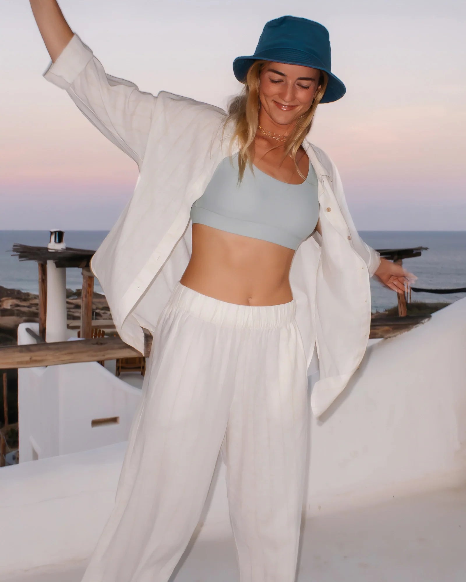 Woman wearing white button-up shirt over light blue bra top in coastal sunset setting