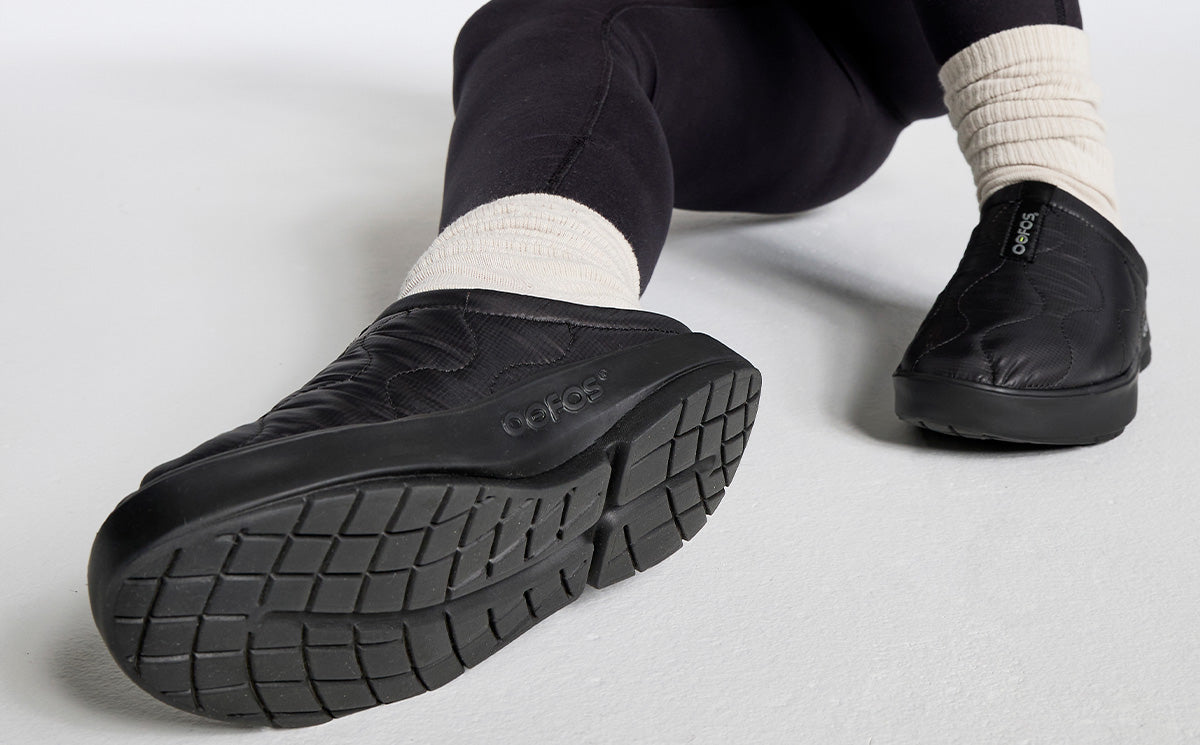 Black quilted slip-on mule shoes shown from sole and side angle on model wearing white socks
