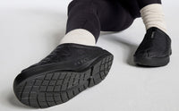 Black quilted slip-on mule shoes shown from sole and side angle on model wearing white socks