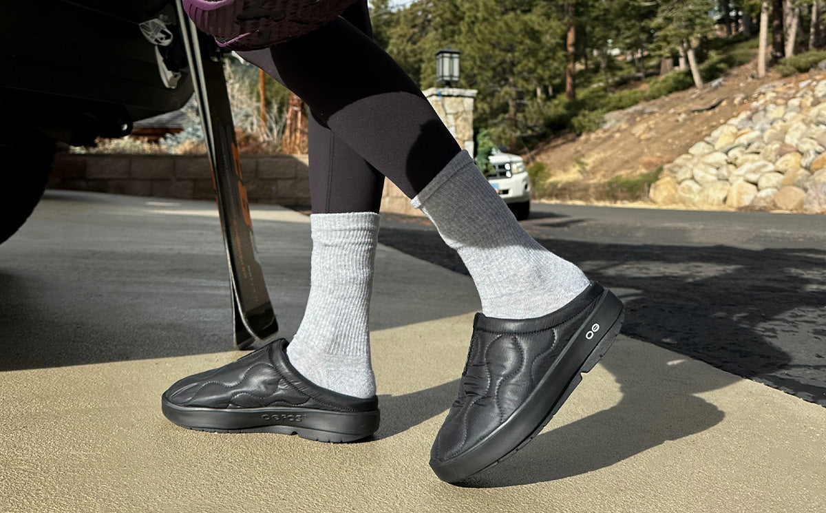 Quilted slip-on mules in black worn with white socks, lifestyle outdoor shot