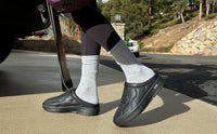 Quilted slip-on mules in black worn with white socks, lifestyle outdoor shot