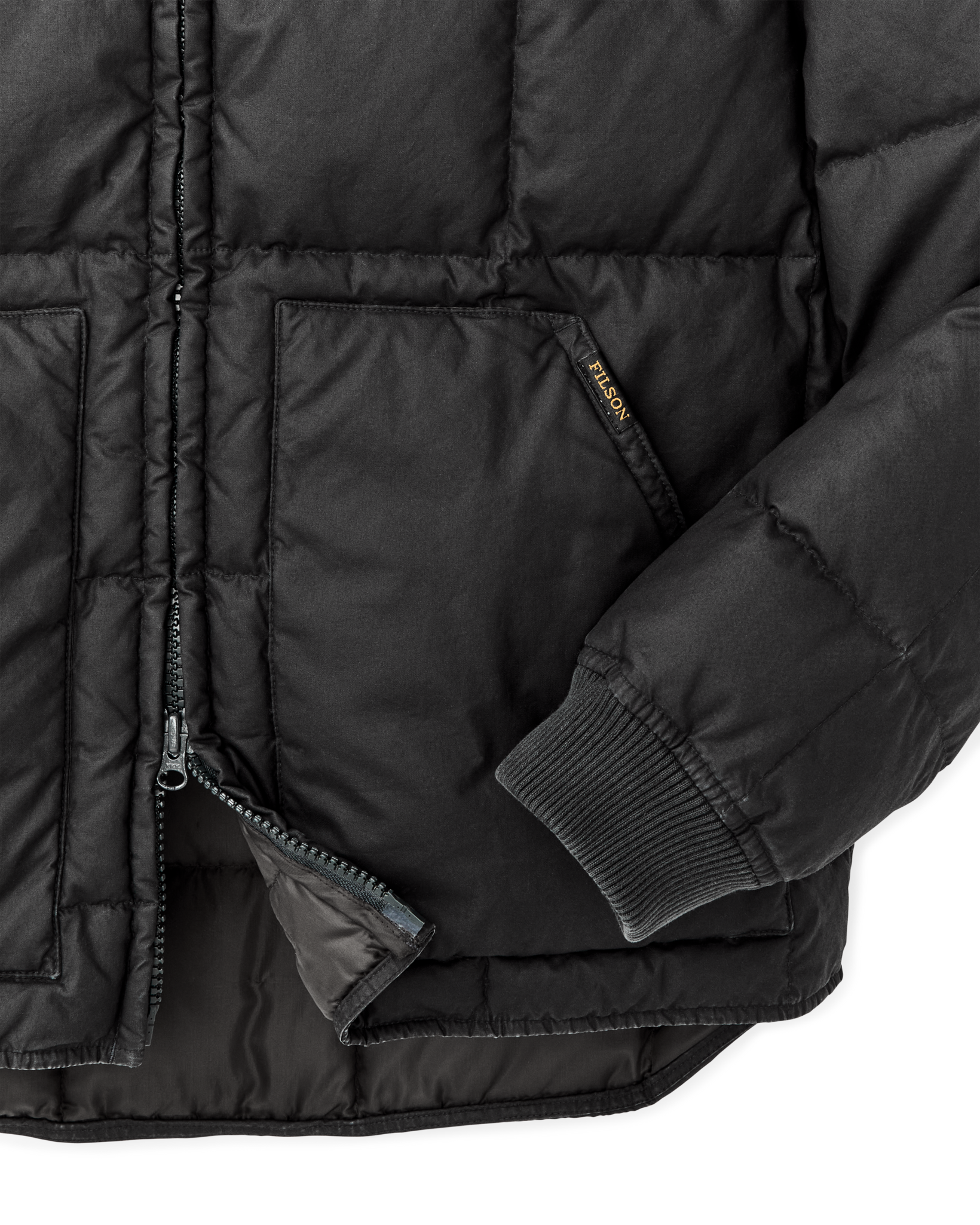 Close-up detail of quilted black down jacket showing zipper, pocket, ribbed cuff, and brand label