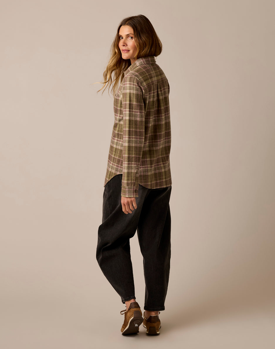 Women's plaid flannel button-up shirt in olive tones, back three-quarter view, paired with dark jeans