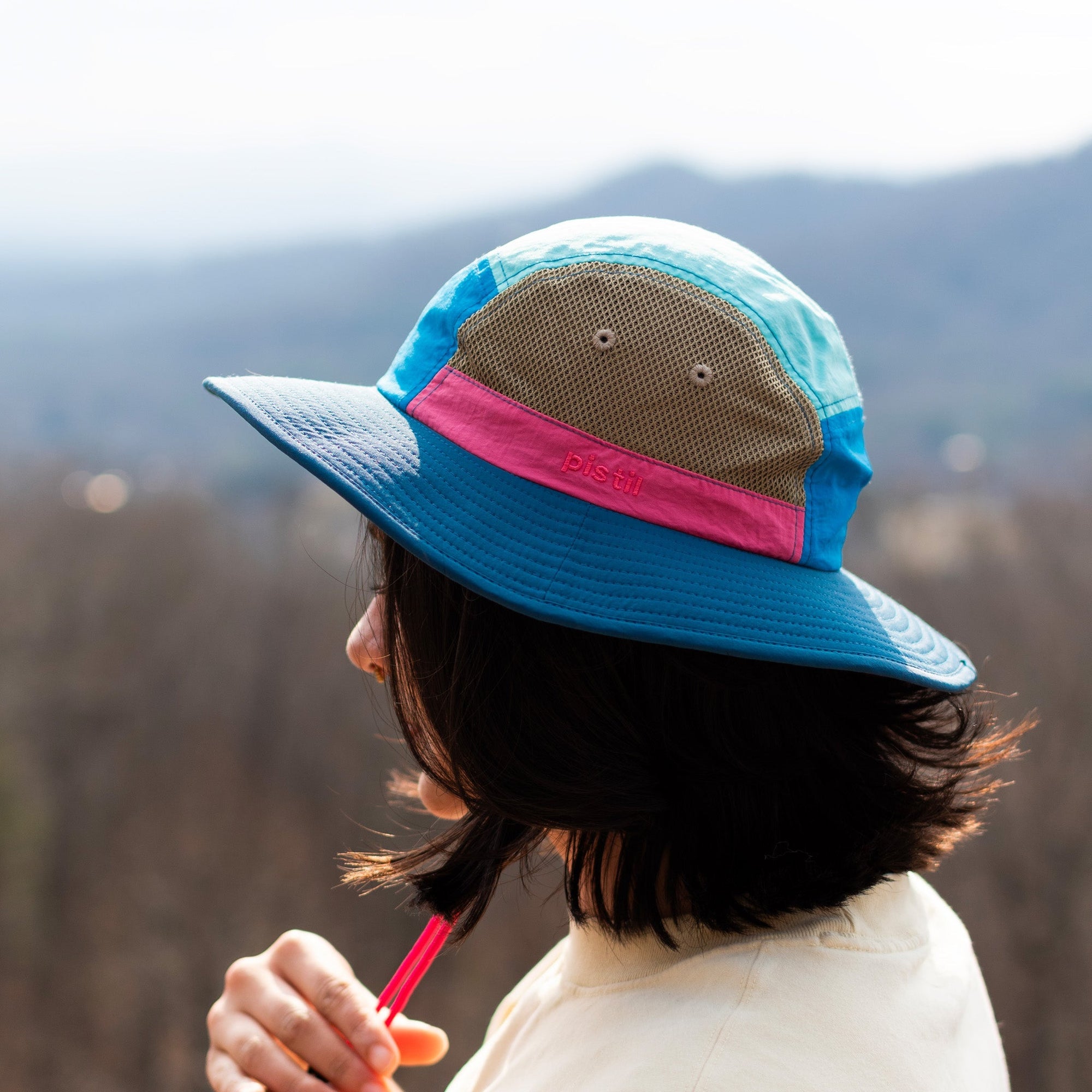 Wide-brim bucket hat with mesh panel, pink band, and blue fabric, side view on model