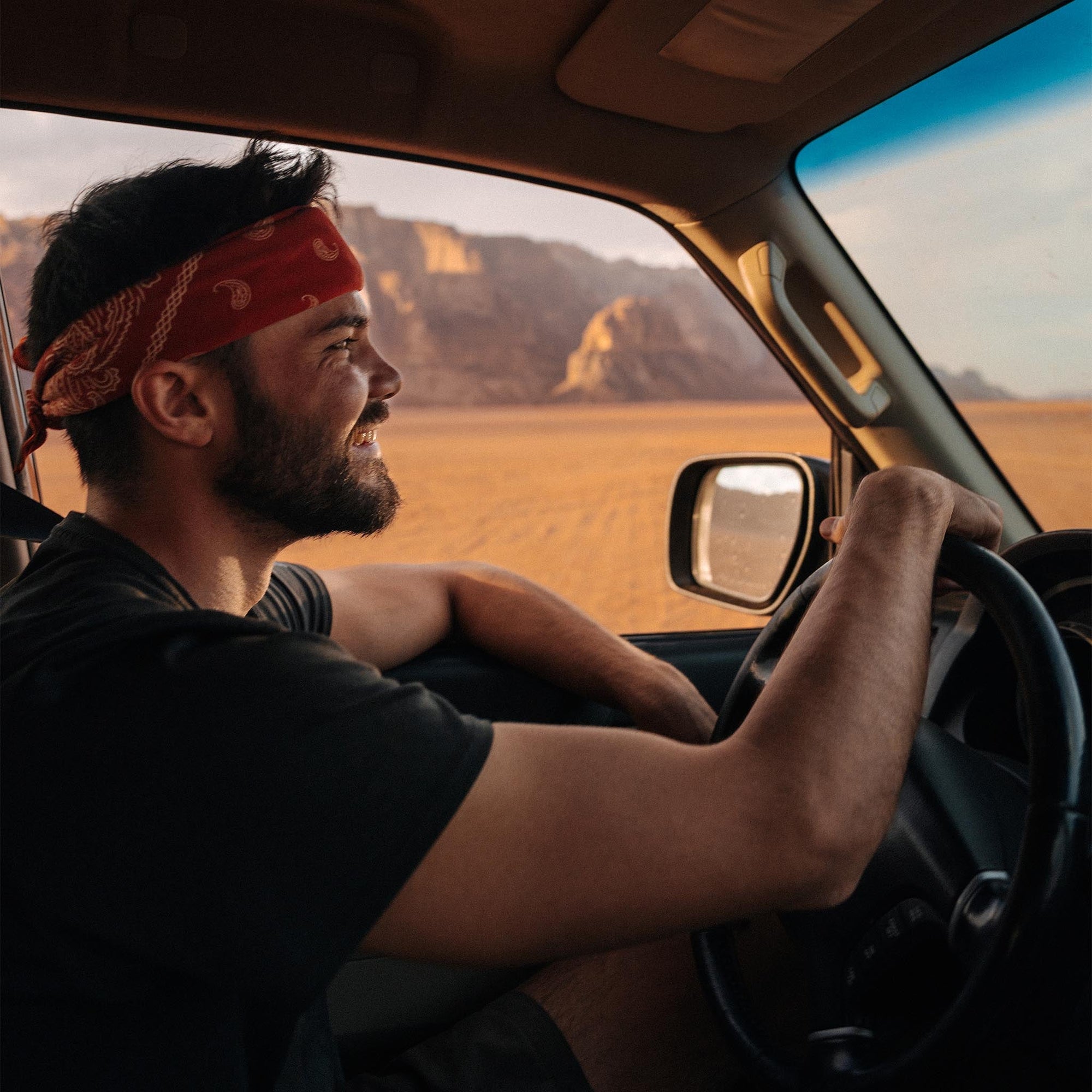 Man wearing red paisley patterned bandana headband while driving in desert landscape