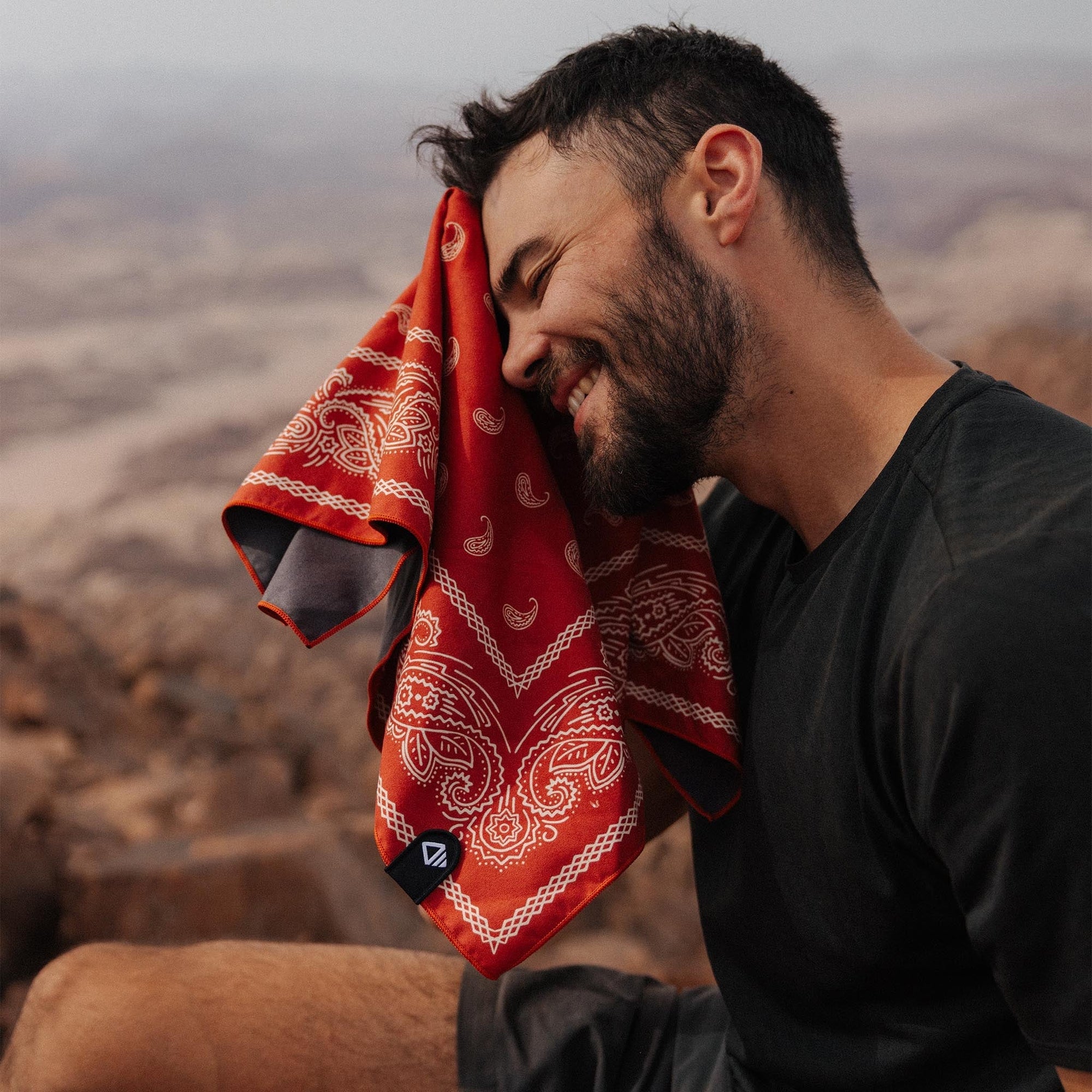 Red bandana towel with white paisley pattern draped over person's head in desert setting