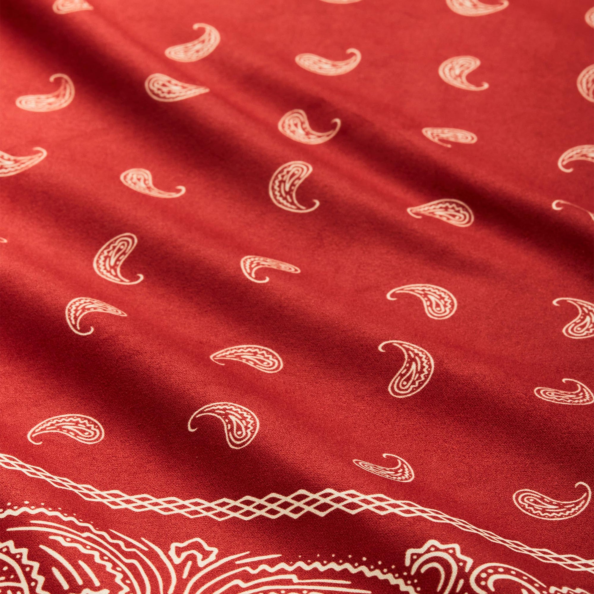 Red bandana towel with white paisley pattern and decorative border, folded fabric view