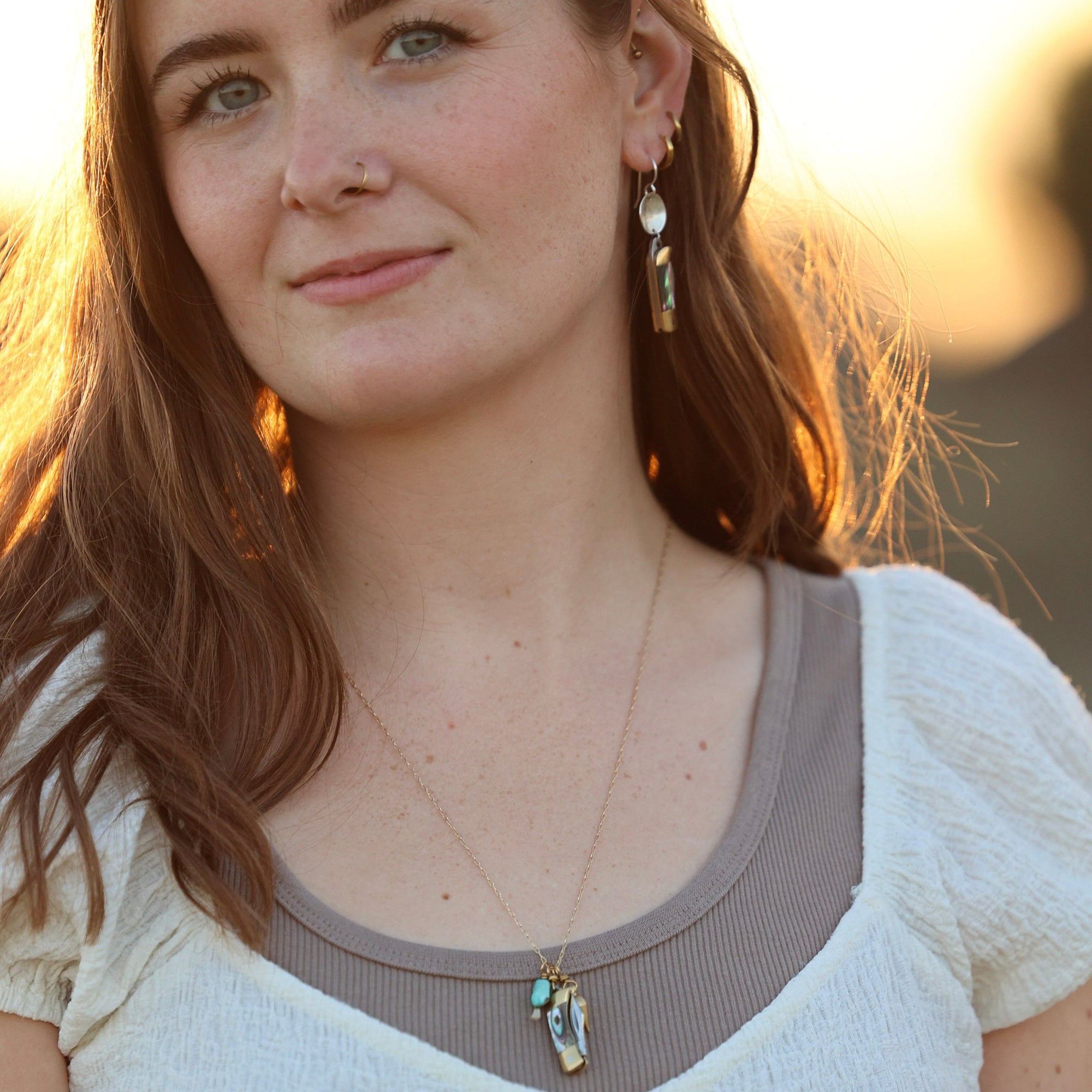 Model wearing dangle earrings with silver disc and iridescent abalone bar pendants, golden hour lighting