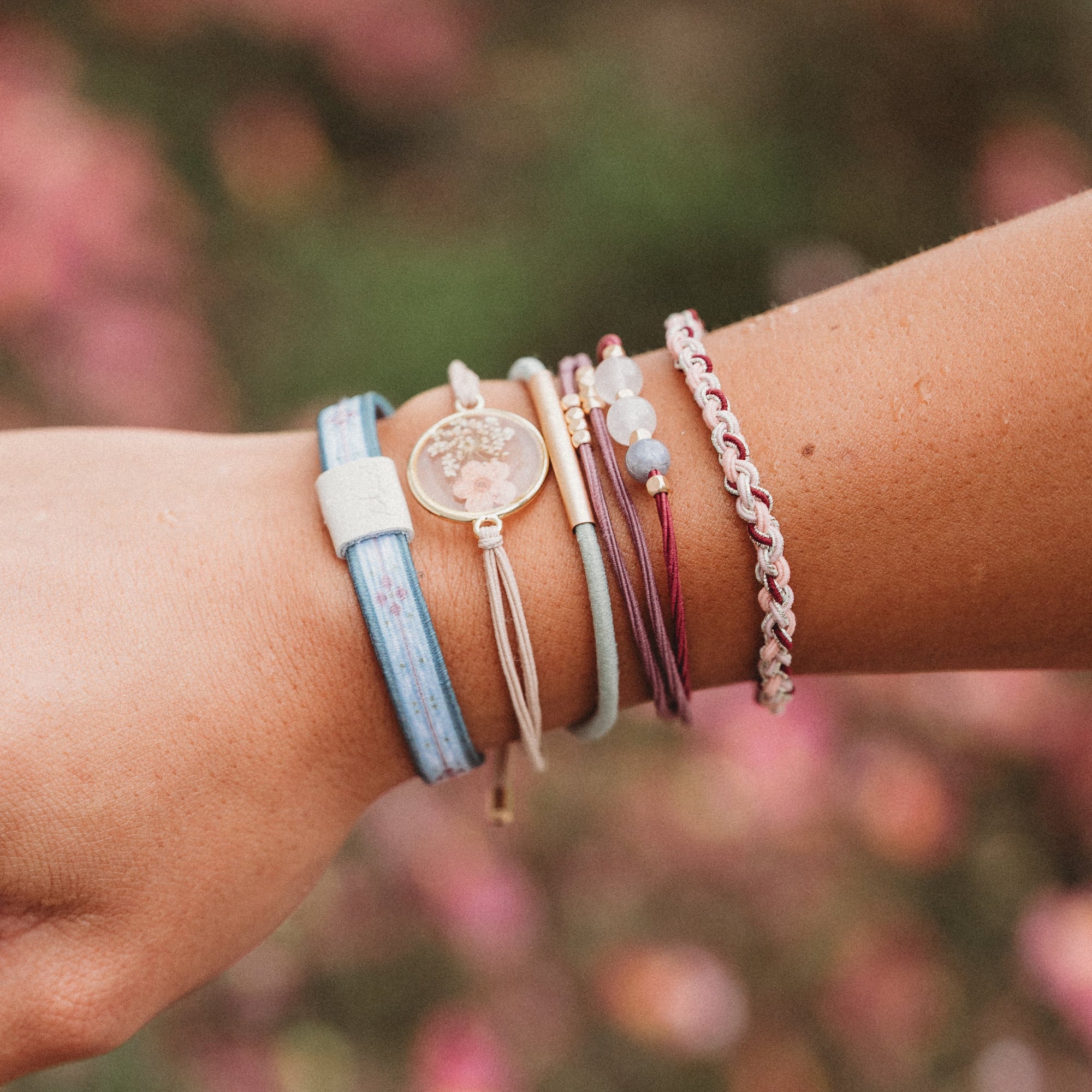 Stacked hair tie and bracelet set on wrist, featuring floral charm, beads, and woven cord styles