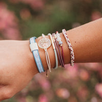 Stacked hair tie and bracelet set on wrist, featuring floral charm, beads, and woven cord styles