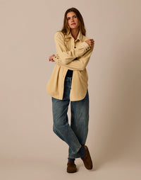 Women's oversized button-up shacket in light beige with chest pockets, worn open over jeans