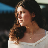 Layered gold necklace set with square engraved pendant worn on model, side profile view