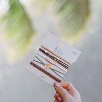 Set of five hair tie bracelets on branded card, featuring braided and cord styles with gold charms