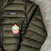 Embroidered cupcake patch with blue frosting on olive green quilted puffer jacket
