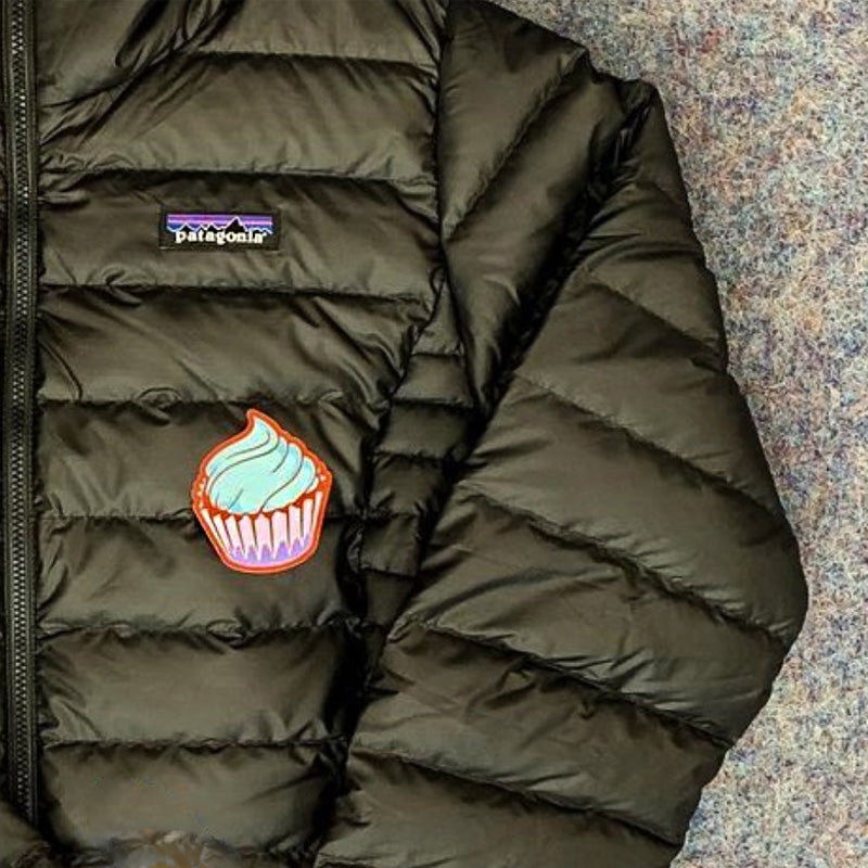 Embroidered cupcake patch with blue frosting on olive green quilted puffer jacket