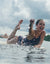 Woman in navy polka dot tankini swimsuit splashing in water with arms raised