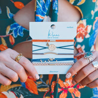 Set of five hair tie bracelets on branded card, featuring braided, cord, and elastic styles with gold accents